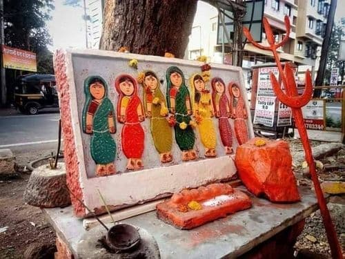 झाडाखालच्या ठाण्यावर वेगवेगळ्या रंगांच्या साड्यांतील सात आसरांचे चित्र आणि शेंदूर लावलेल्या शिळा
